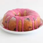 Lemon ricotta blueberry bundt cake with pink blueberry glaze dripping down the sides on a white plate