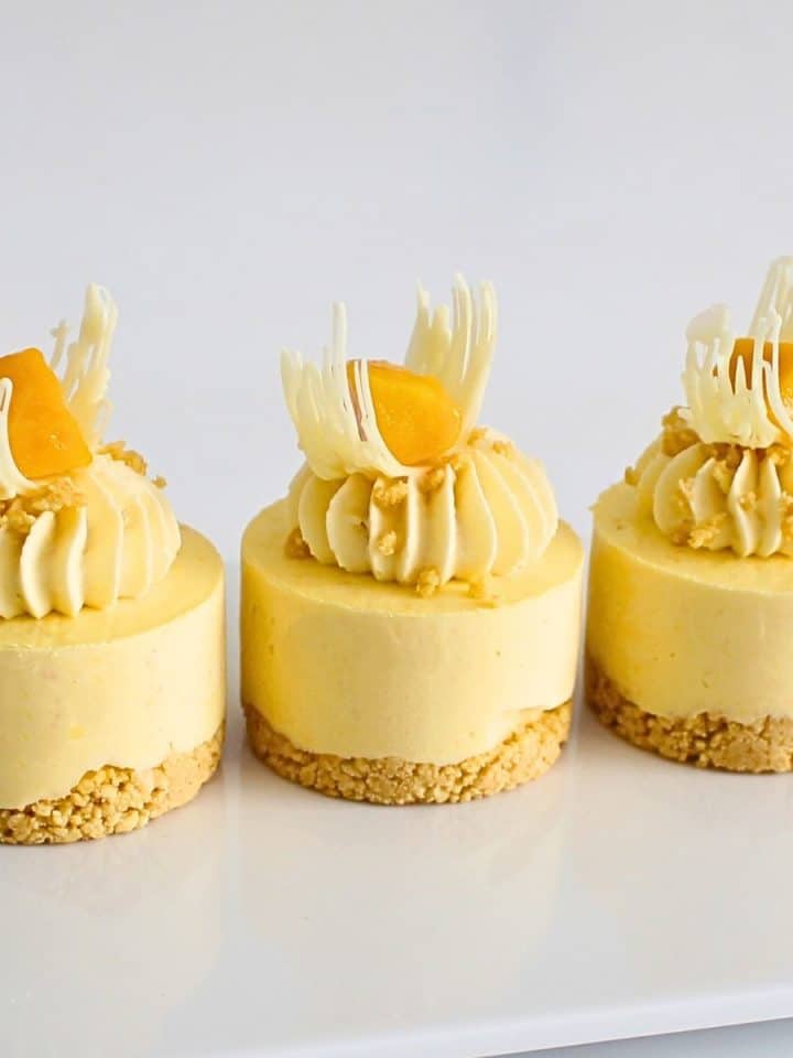 Mini mango cheesecakes with mango topping on a cookie crust, chilled and served on a white plate
