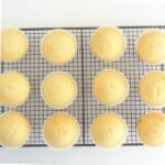 Moist vanilla cupcakes in baking cups cooling on wire rack