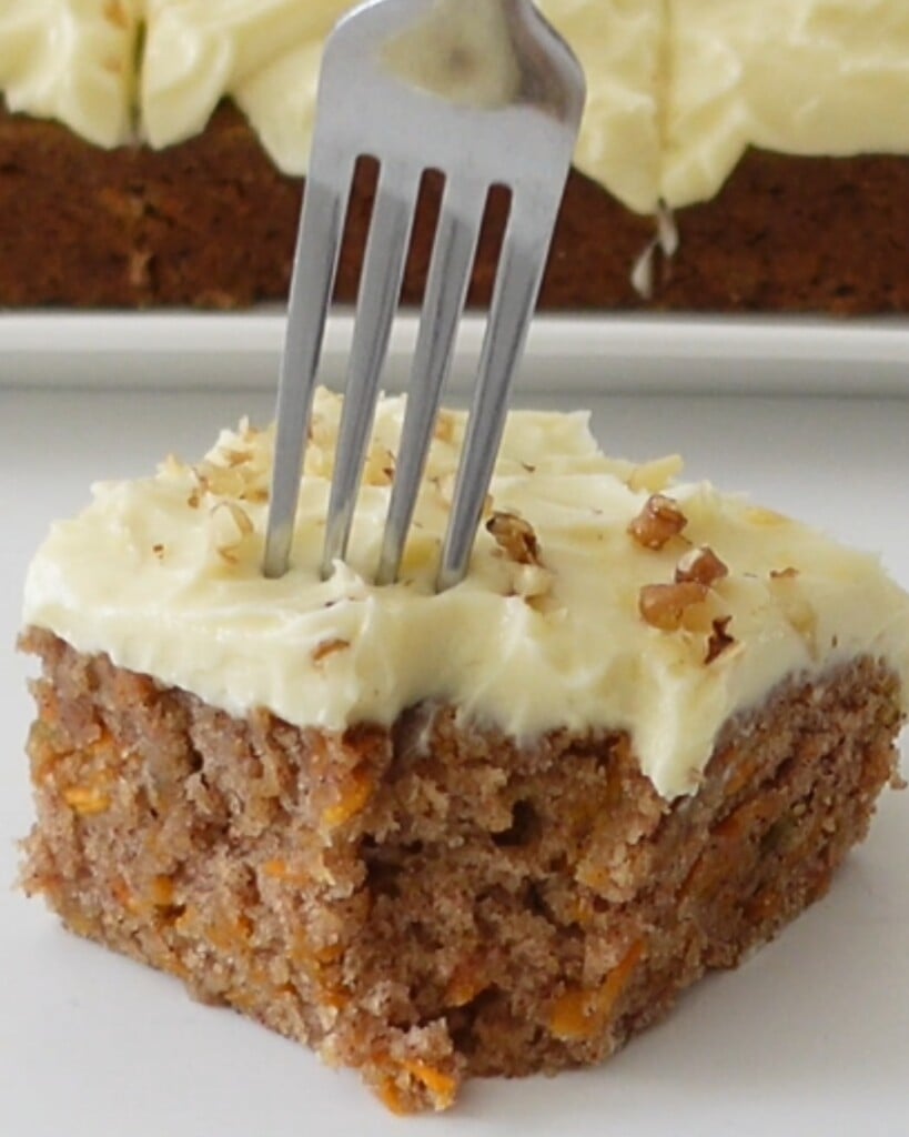 Fork cutting through a moist slice of eggless carrot cake with frosting