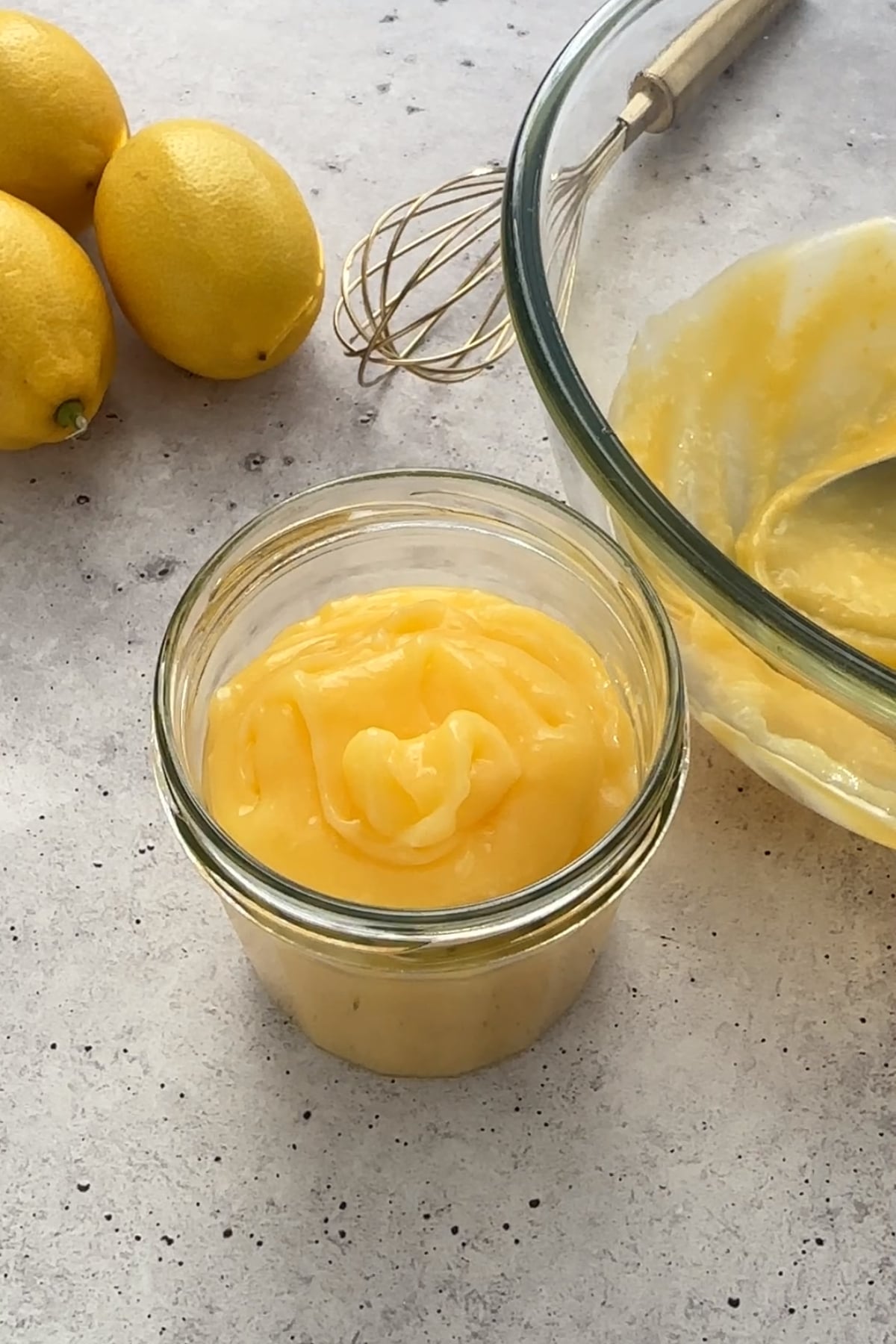 Glass jar filled with lemon curd, fresh lemons beside ir