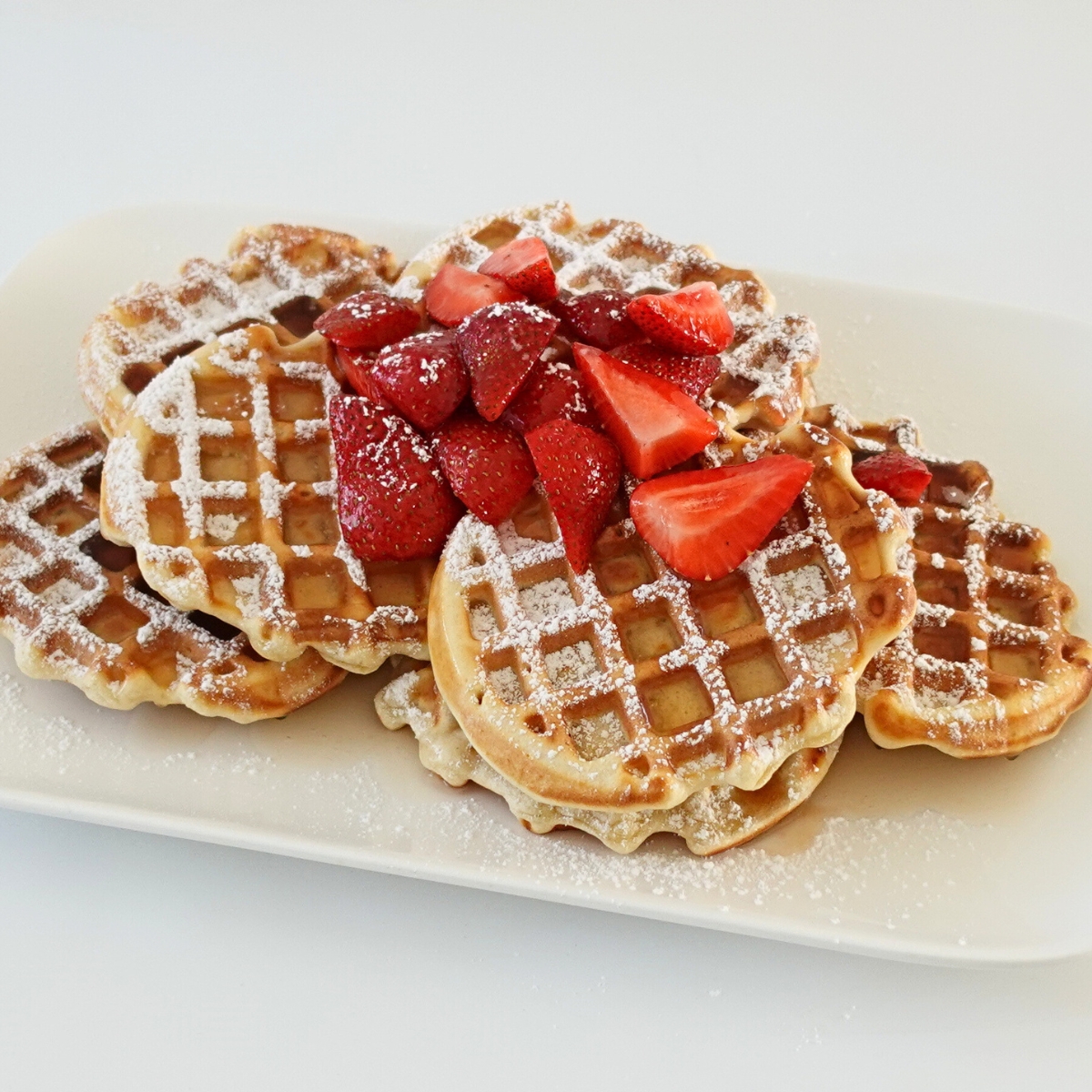 Golden mini waffles made in a mini waffle maker served with fresh strawberries and syrup