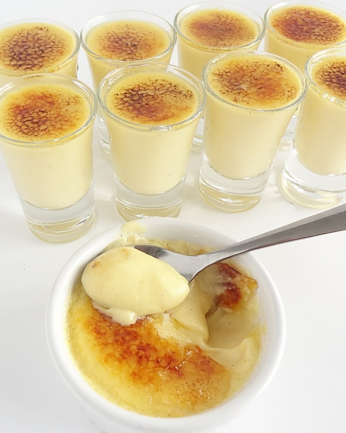 spoon scooping creamy no bake crème brûlée custard from ramekin with caramelized sugar top and mini shot glasses in background