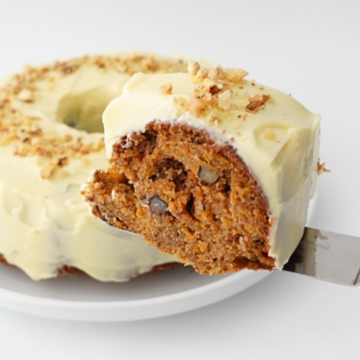 Slice of moist carrot cake topped with cream cheese frosting and chopped walnuts