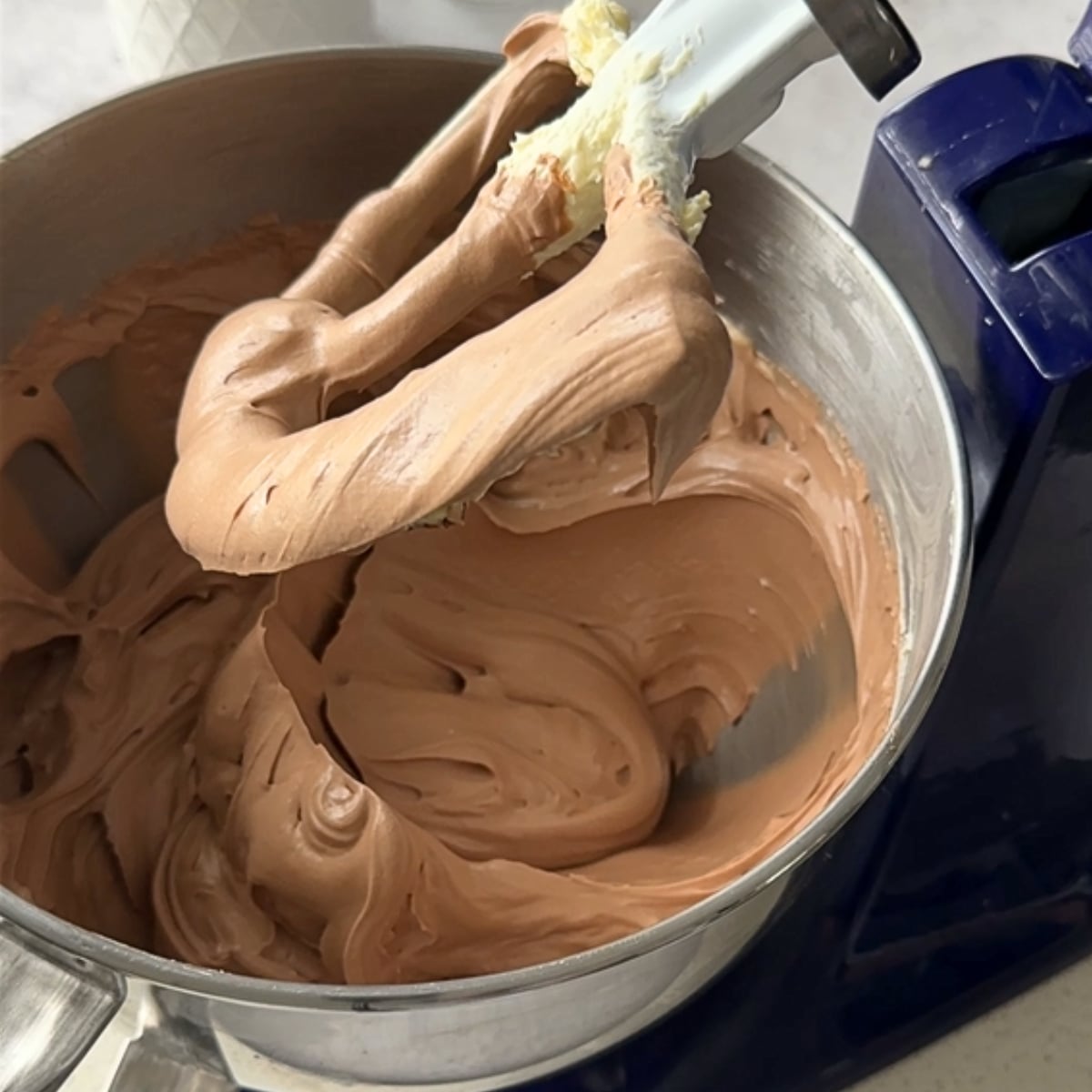 Melted chocolate being mixed into buttercream in a stand mixer