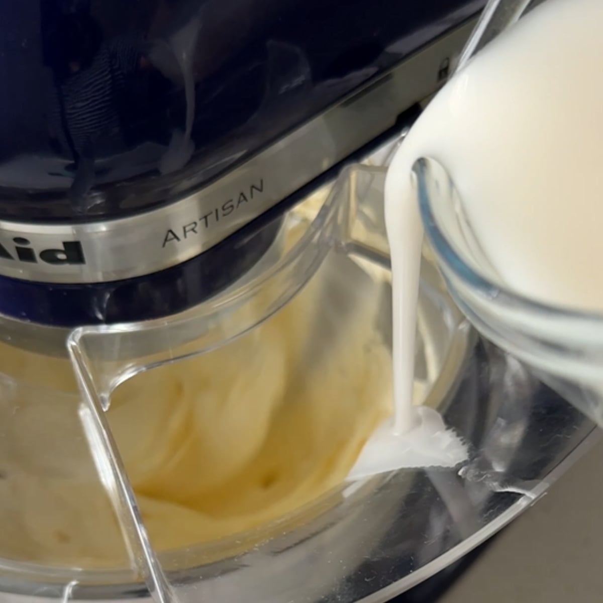 Sugar mixture being poured into whipped butter in a stand mixer