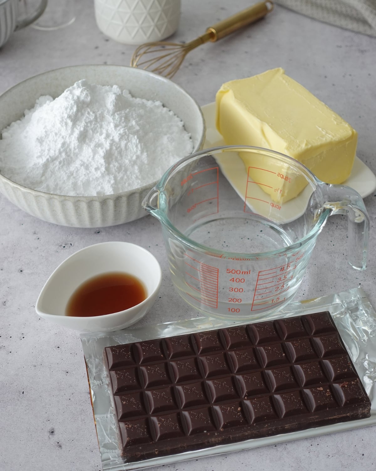 Butter, powdered sugar, vanilla, and a bar of dark chocolate on a kitchen counter