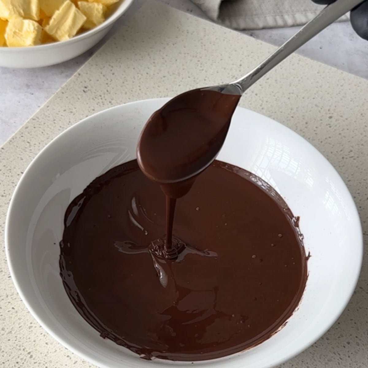 Melted chocolate being drizzled from a spoon in a white bowl