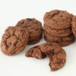 Stack of chocolate cake mix cookies with one cookie broken in half showing melty chocolate chips and chunks inside