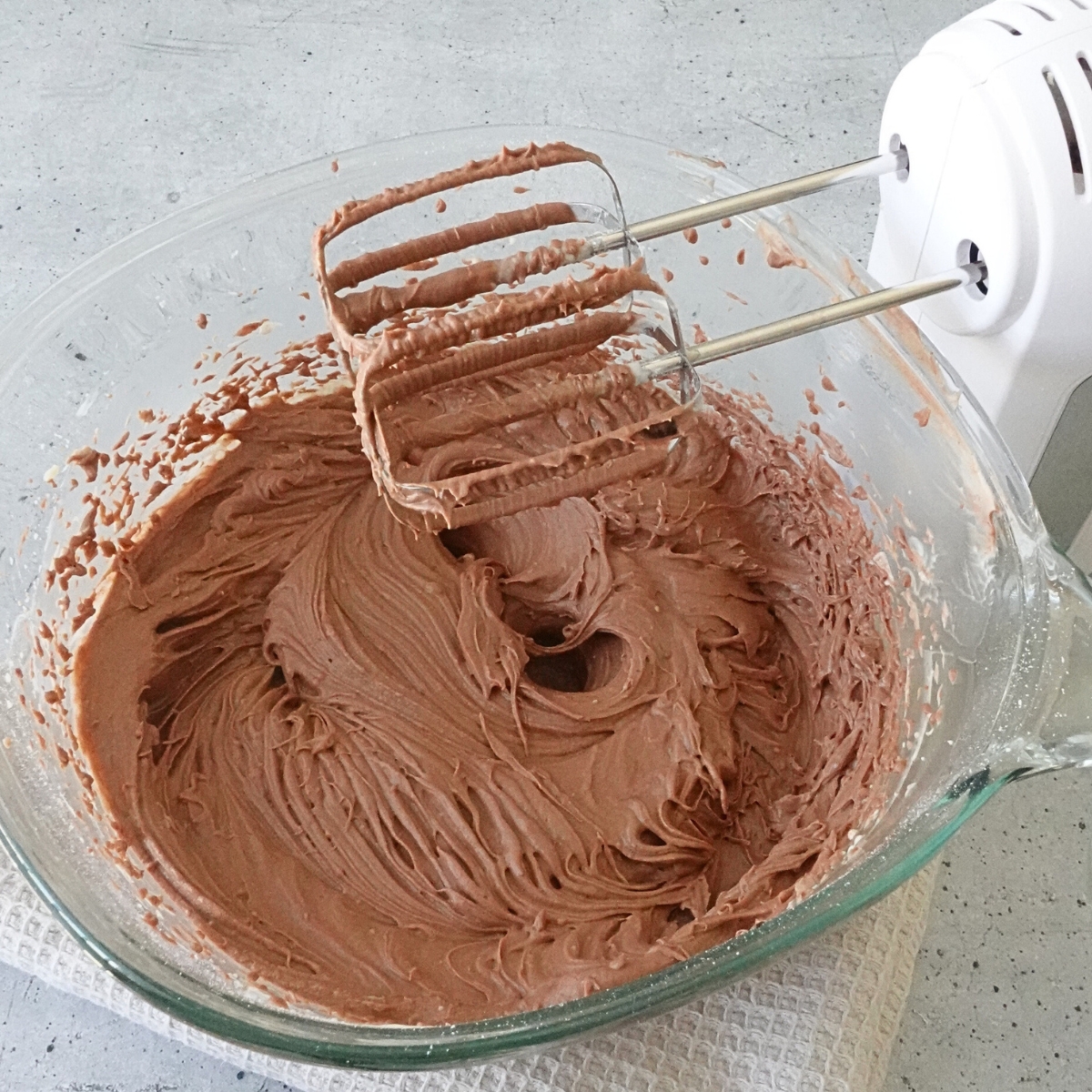 Smooth and thick chocolate cream cheese frosting in a glass bowl with hand mixer beaters after mixing