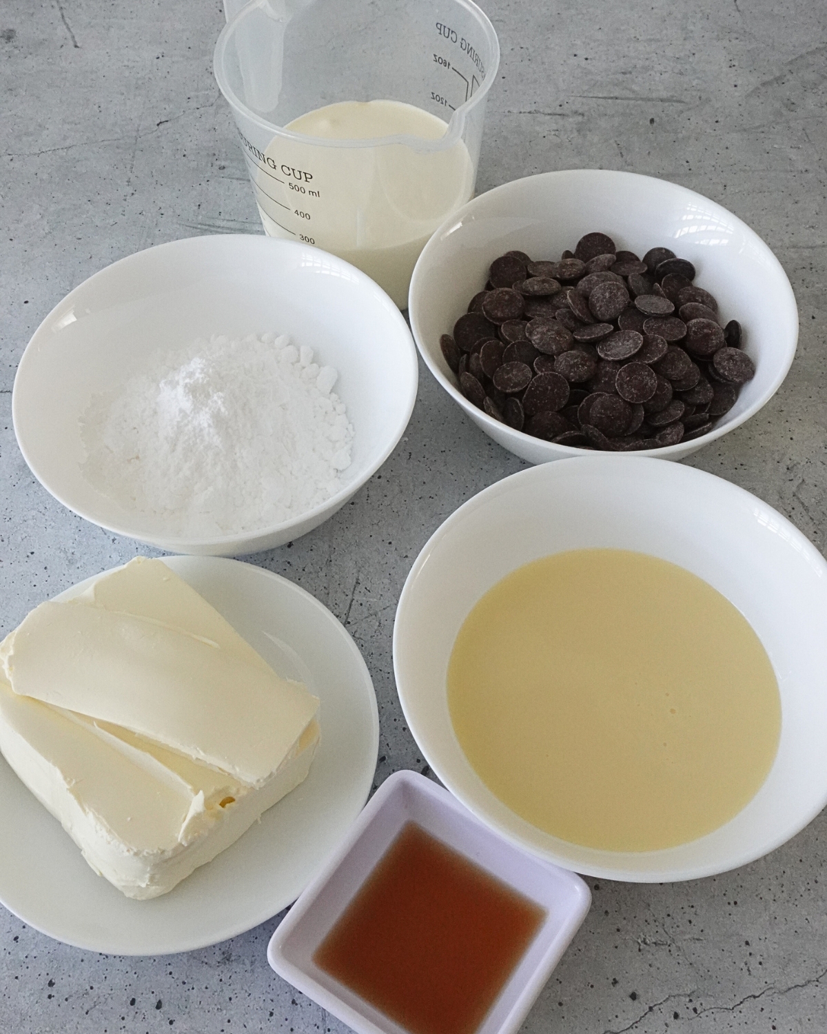 Ingredients for chocolate cream cheese frosting including cream cheese, dark chocolate, condensed milk, powdered sugar, cream, and vanilla extract