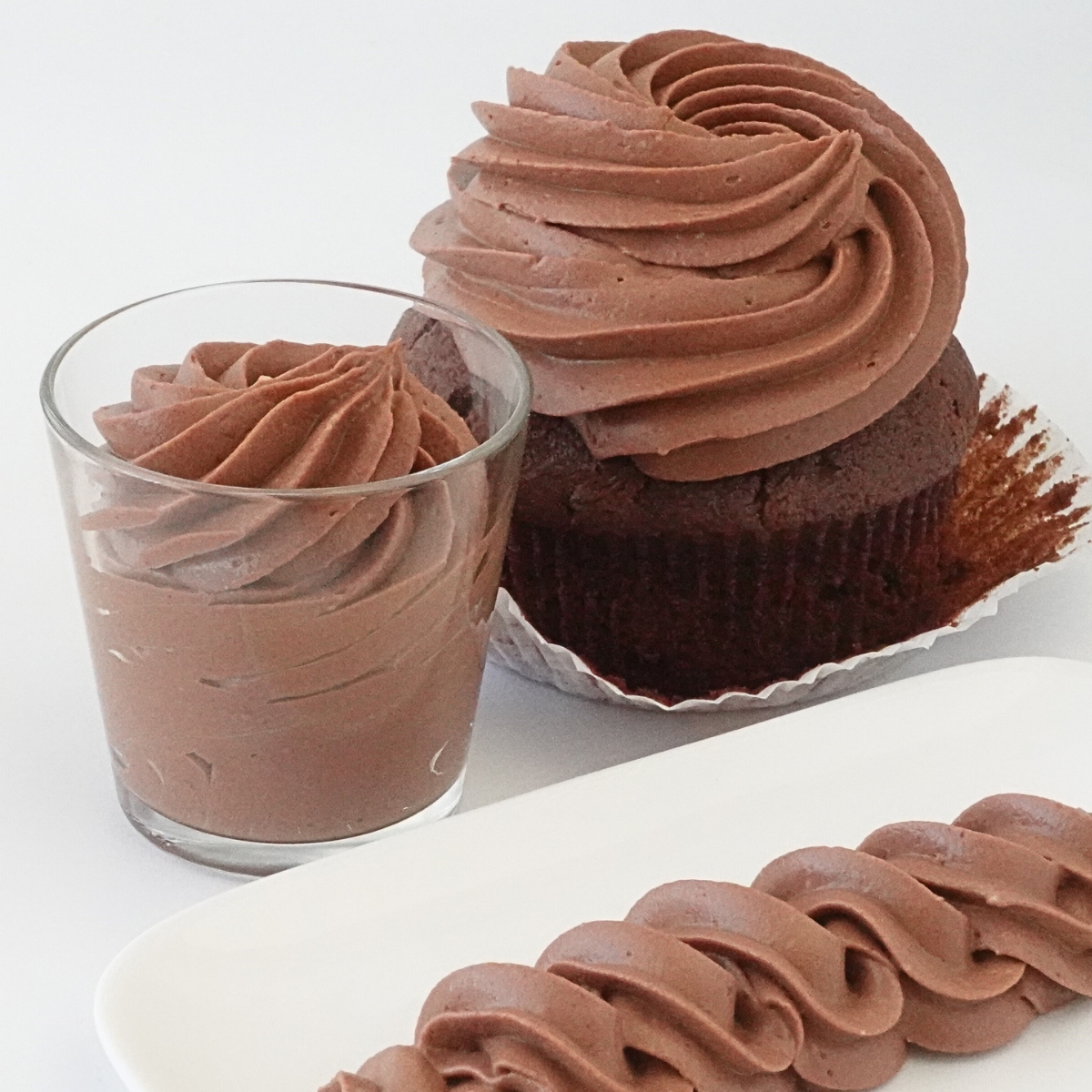 Silky chocolate cream cheese frosting piped on a chocolate cupcake and swirled in a glass cup