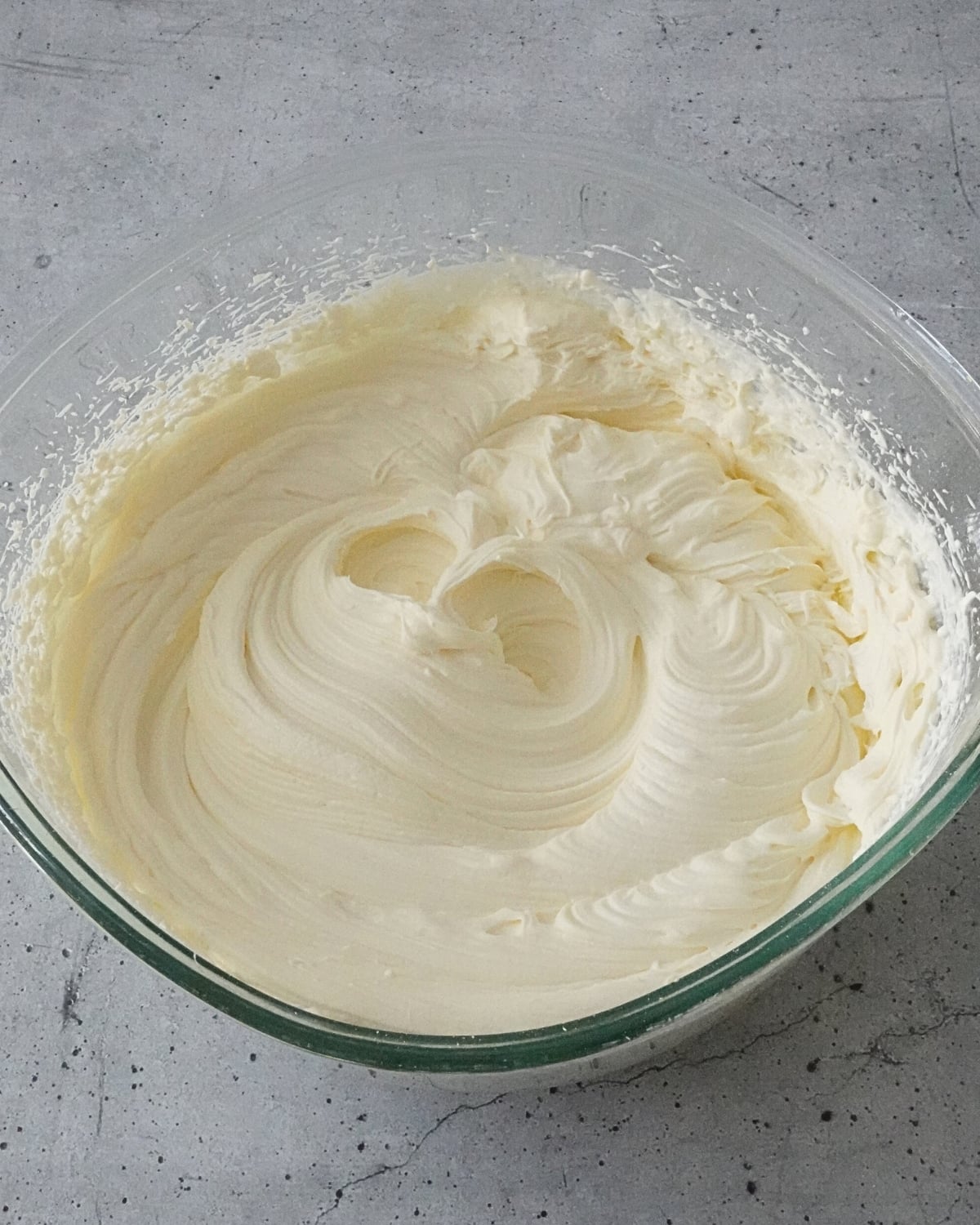 Smooth and fluffy cream cheese frosting whipped to firm peaks in a glass mixing bowl on a grey surface