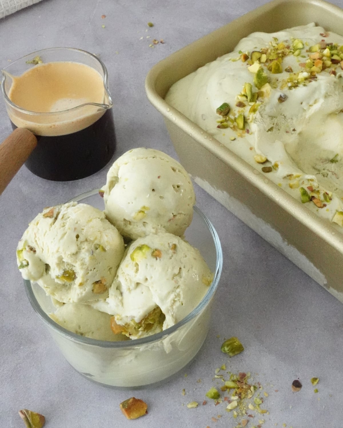 Bowl of creamy pistachio ice cream with chopped pistachios beside a loaf pan filled with ice cream and an espresso shot for affogato