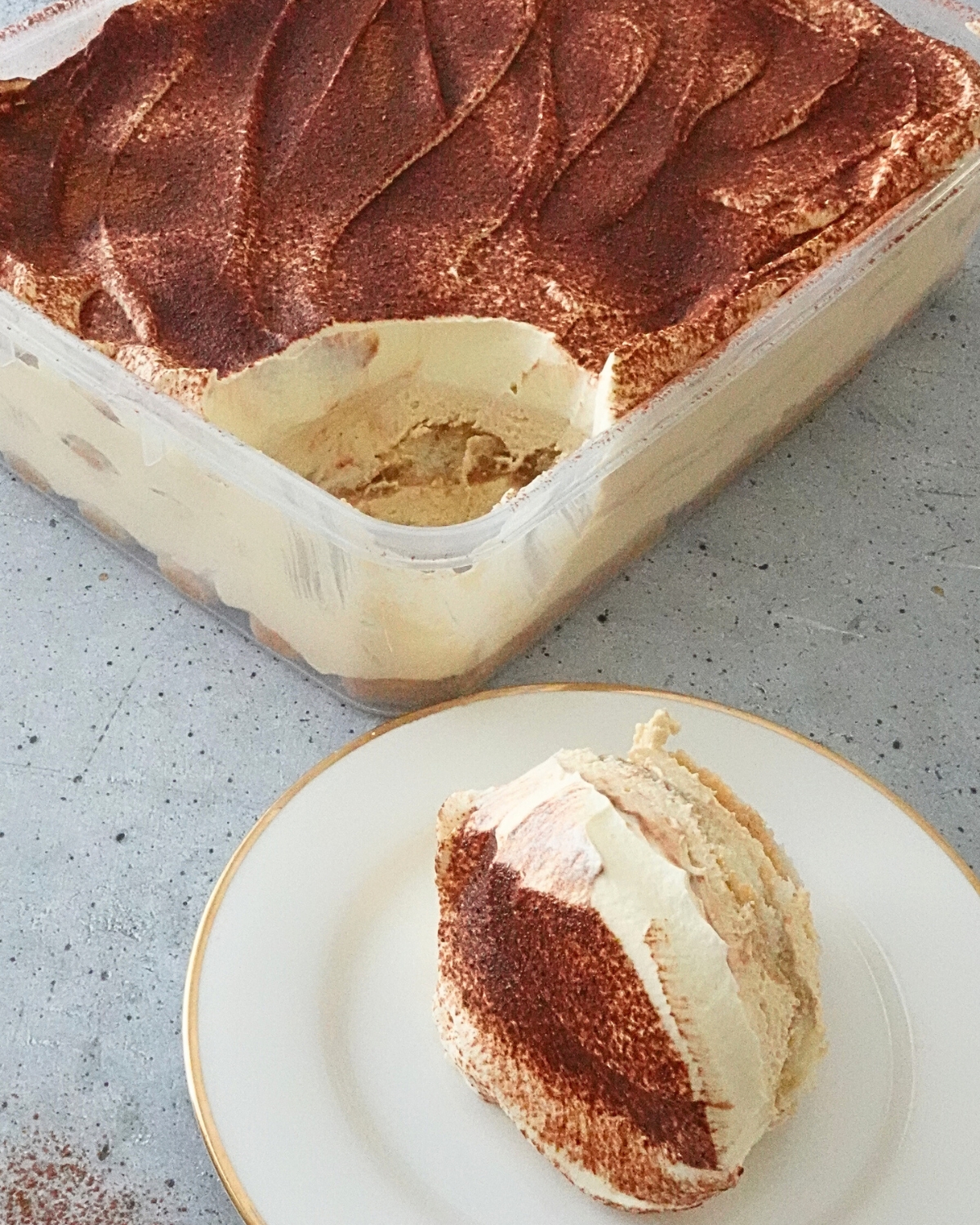 tiramisu cheesecake in a tray with cocoa dusting and a slice served on a plate