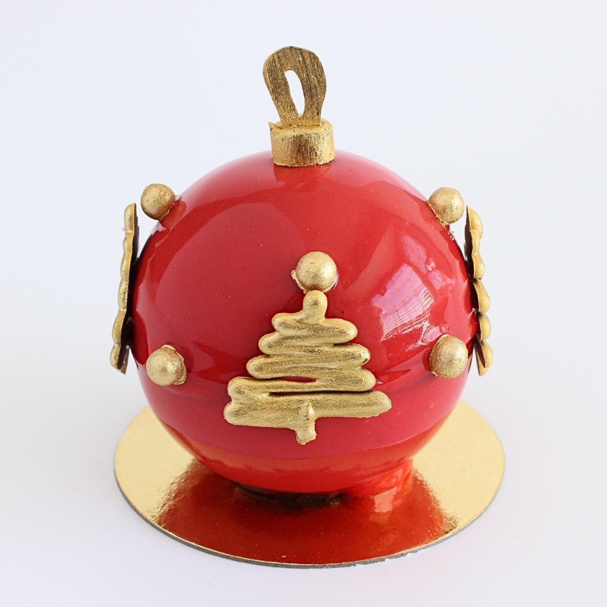 Shiny red mirror glaze Christmas ornament dessert with gold chocolate decorations on a small gold cake board.