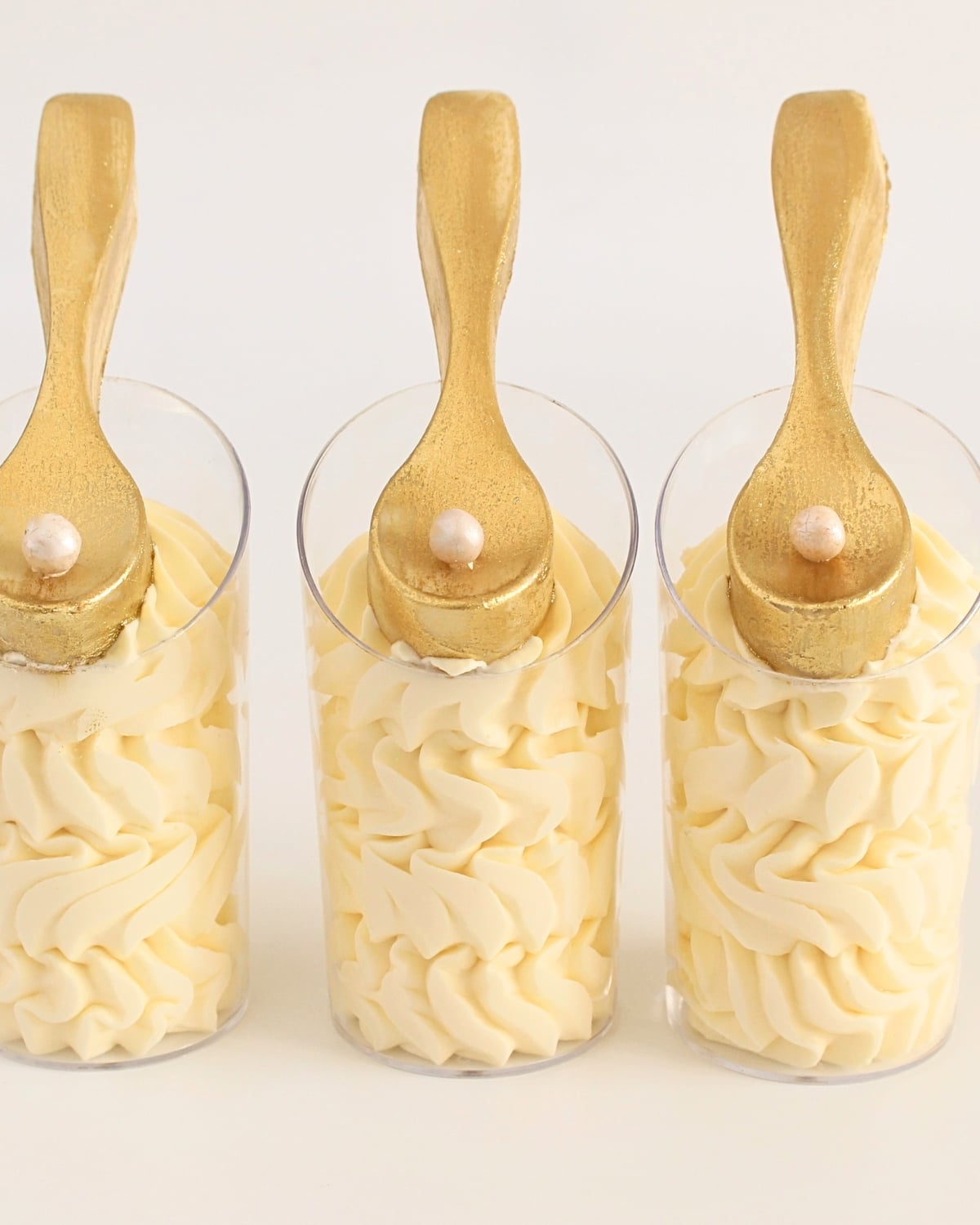 White chocolate mousse cups with smooth piped layers, topped with edible gold chocolate spoons.
