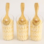 White chocolate mousse cups piped with creamy layers and topped with edible gold chocolate spoons.