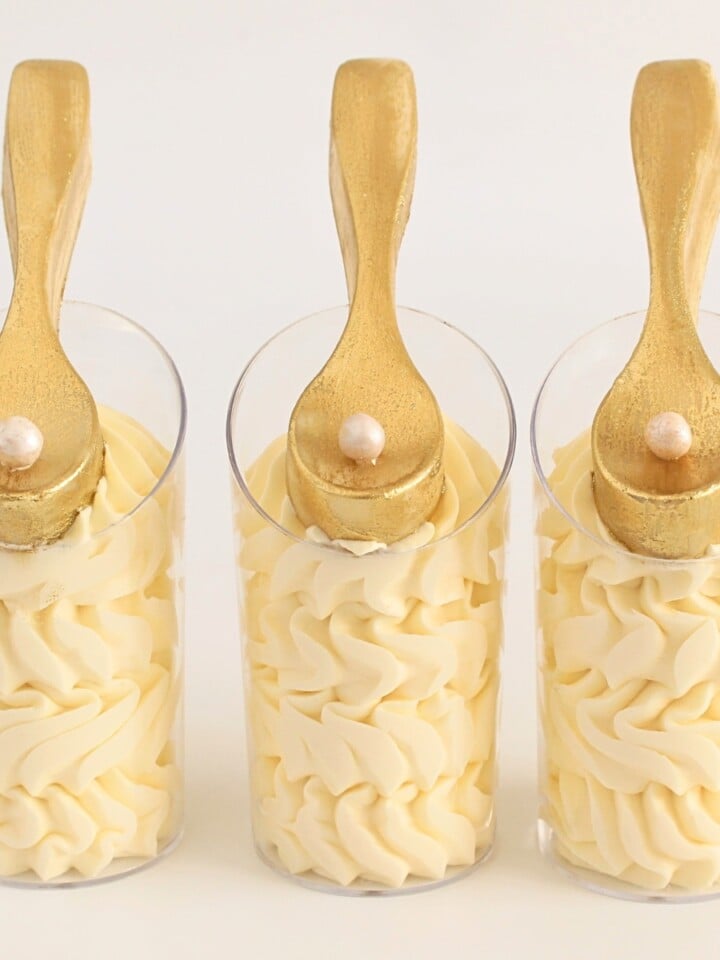 White chocolate mousse cups piped with creamy layers and topped with edible gold chocolate spoons.