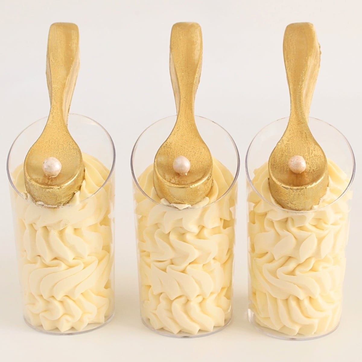 White chocolate mousse cups piped with creamy layers and topped with edible gold chocolate spoons.