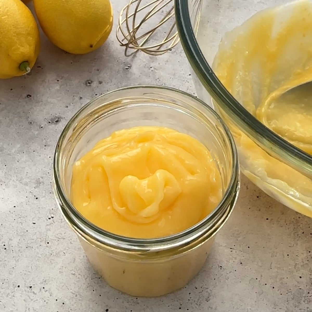 Whole Egg Lemon Curd in a glass jar, fresh lemons beside it