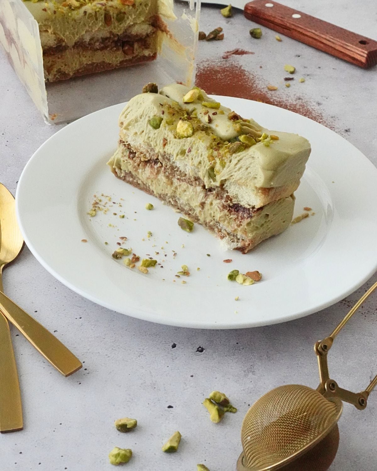A slice of no-bake pistachio tiramisu cheesecake on a plate, showing layers of ladyfingers and pistachio filling