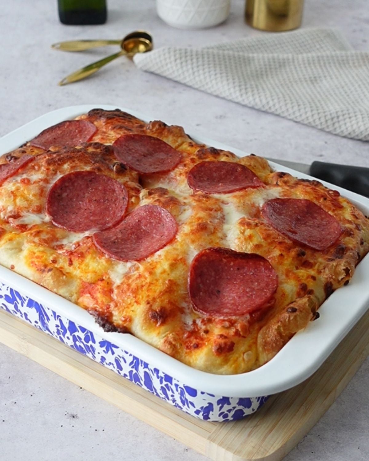 Baked focaccia pizza topped with pizza sauce, melted cheese, and salami slices in a blue and white baking dish