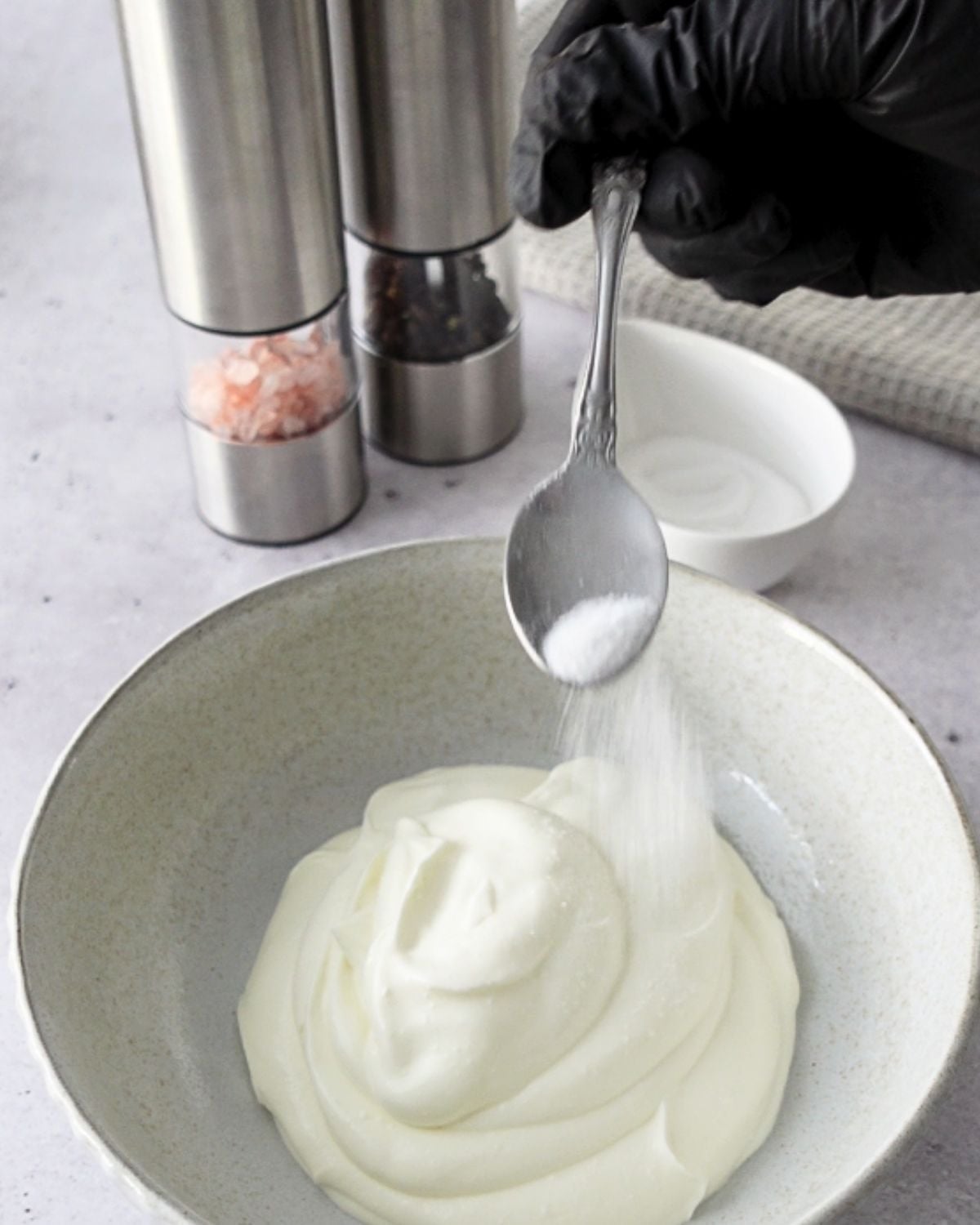 Salt being sprinkled over Greek yogurt in a bowl