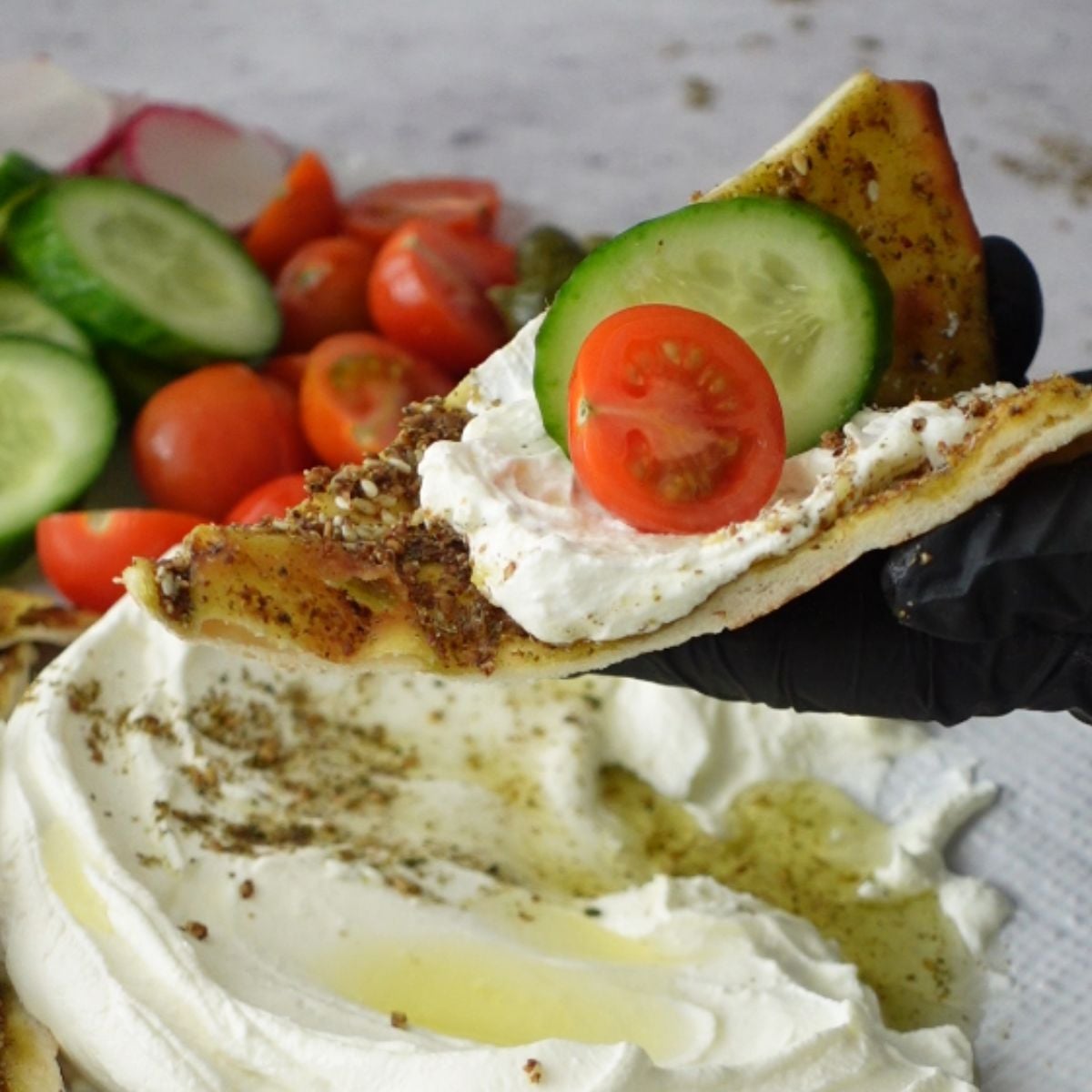 Za'atar manoosh topped with labneh dip, tomato, and cucumber