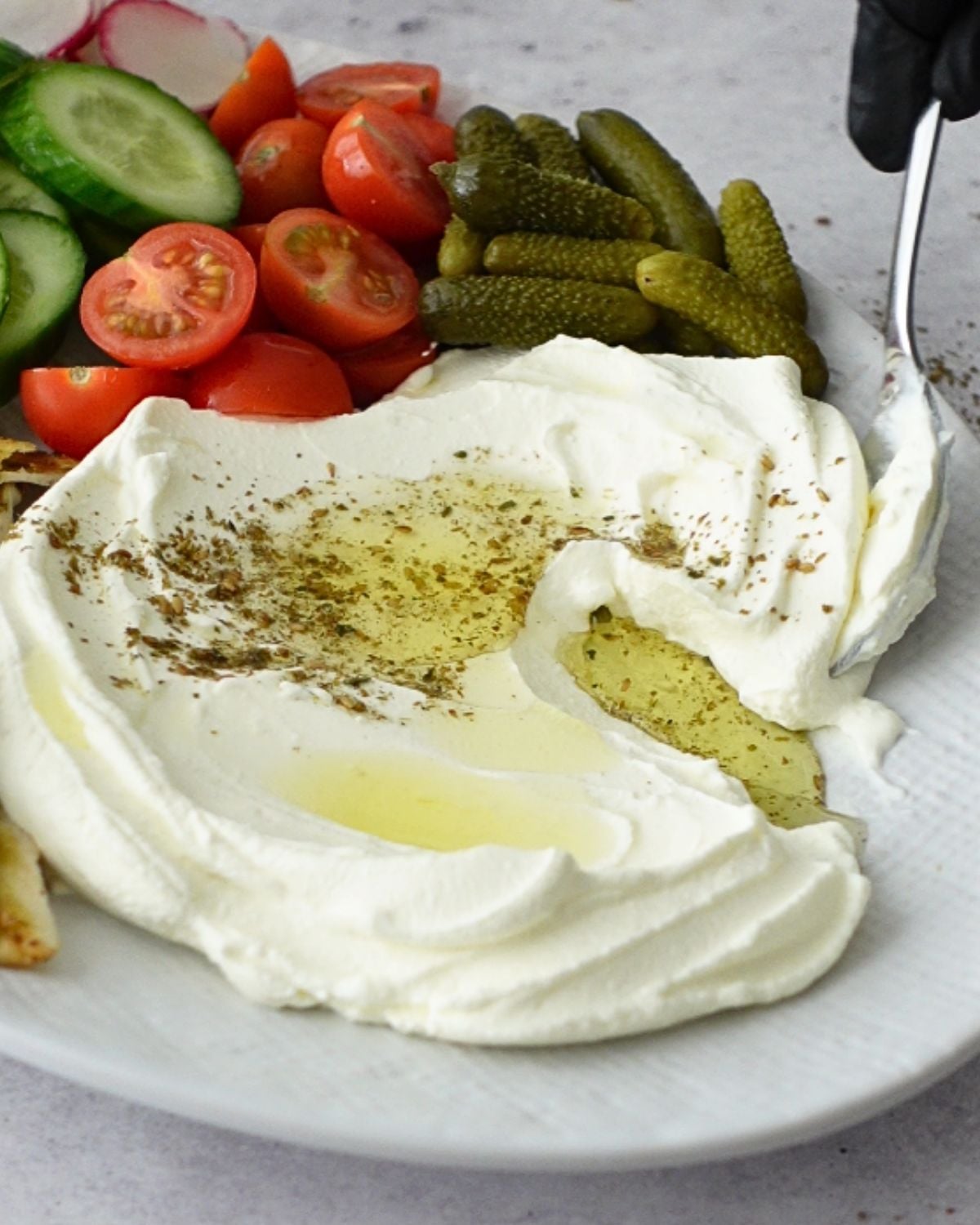 Scooping labneh dip topped with olive oil and za'atar from a platter