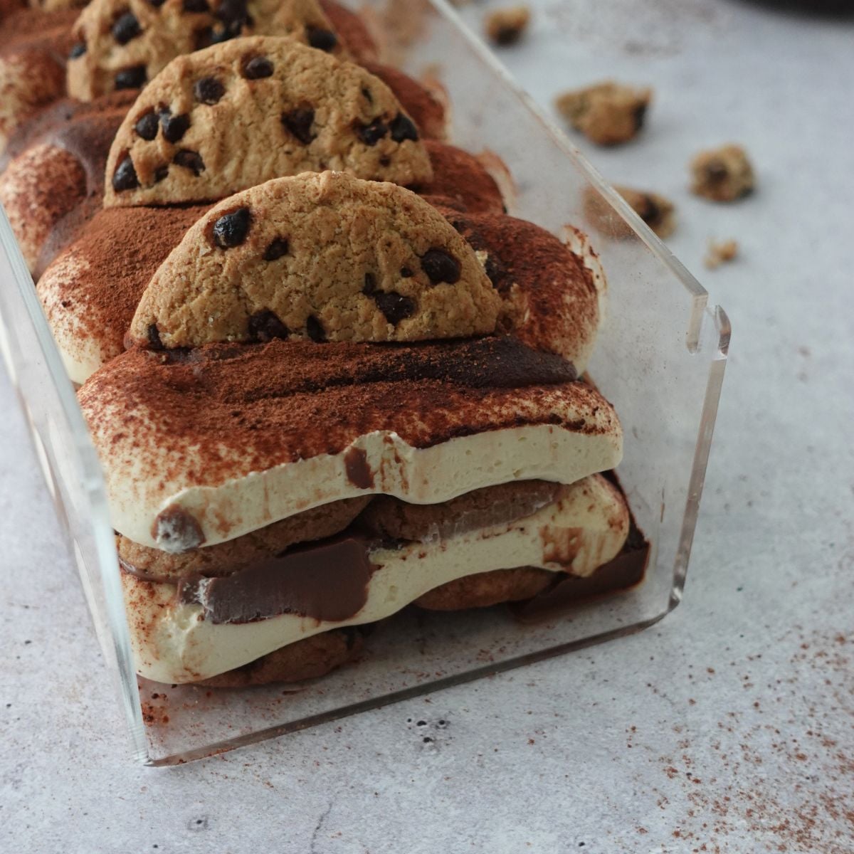 No-bake chocolate chip tiramisu cheesecake in a loaf pan, layered with cocoa powder and topped with chocolate chip cookies