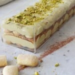 No-bake pistachio tiramisu cheesecake in a loaf pan, topped with crushed pistachios and cocoa powder