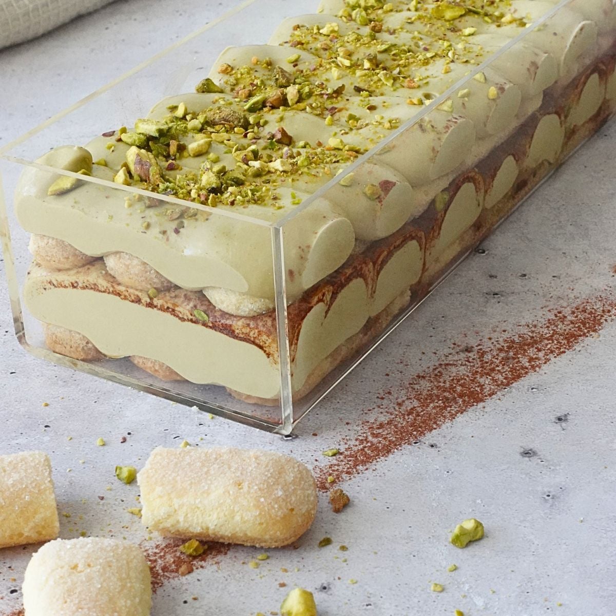 No-bake pistachio tiramisu cheesecake in a loaf pan, topped with crushed pistachios and cocoa powder