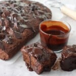 Same-day chocolate focaccia on parchment paper with ganache drizzled over the top, two slices cut showing the chocolate crumb, and a glass of ganache on the side