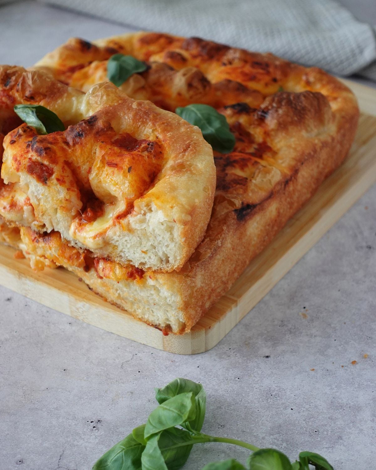 Same-day focaccia pizza base sliced on a wooden board showing the thick airy crumb and golden crust topped with bocconcini and fresh basil