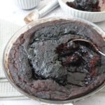 Chocolate self saucing pudding in a pie dish with a spoon through the center showing the sauce underneath