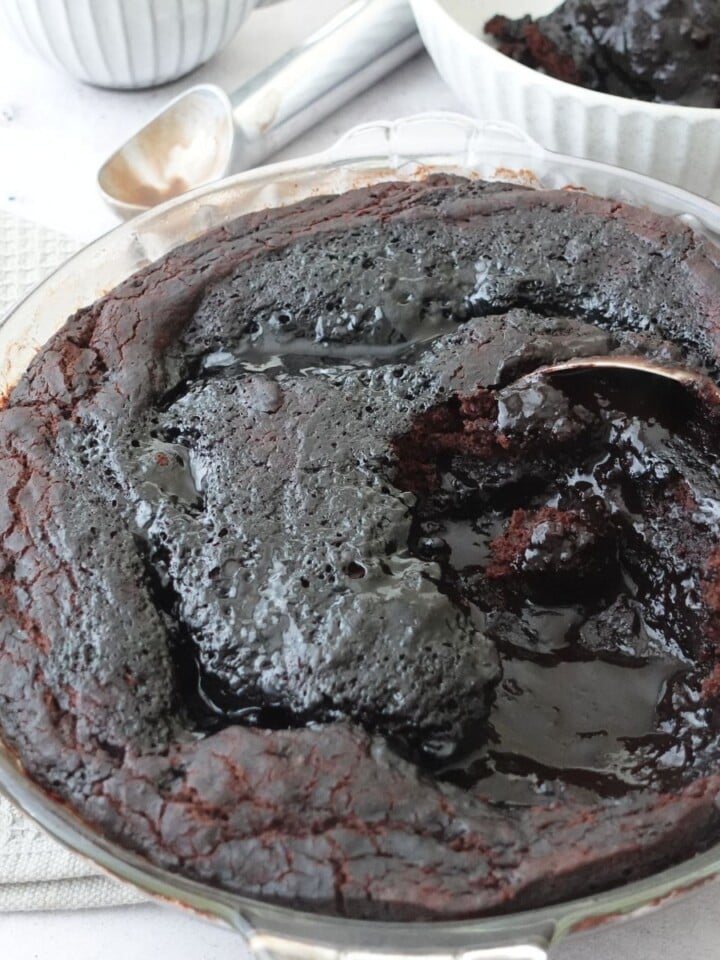 Chocolate self saucing pudding in a pie dish with a spoon through the center showing the sauce underneath