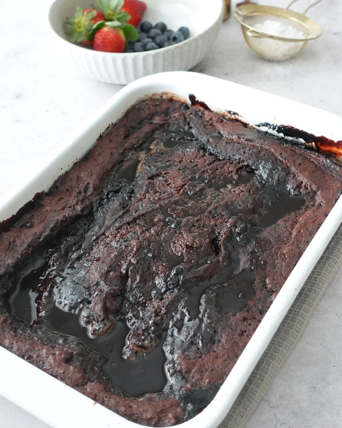 Chocolate self saucing pudding baked in a white dish with fresh berries alongside