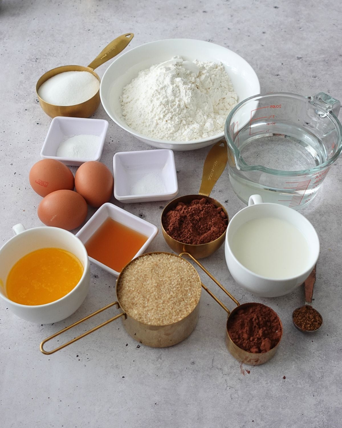 Ingredients for chocolate self saucing pudding measured out, including flour, cocoa powder, brown sugar, eggs, butter, milk, vanilla and instant coffee
