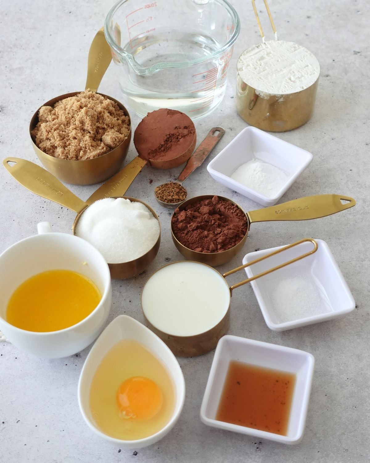 Ingredients for chocolate self saucing pudding measured out in bowls and cups, including brown sugar, cocoa powder, flour, milk, butter, egg, vanilla and instant coffee granules