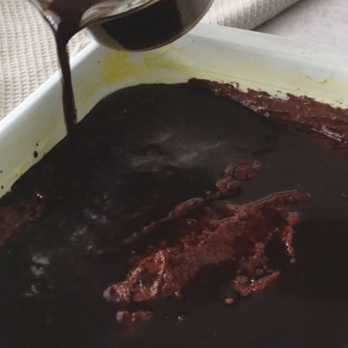 Chocolate sauce mixture being poured over pudding batter in a baking dish