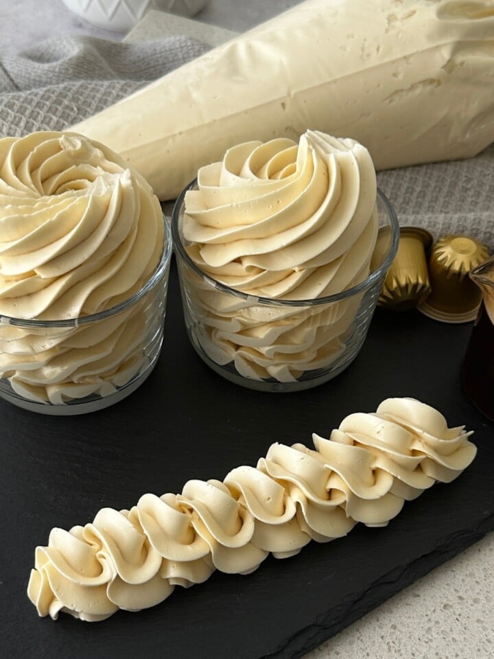 Coffee hot water buttercream piped into swirls in glass jars with a rope border and espresso pods on a slate board