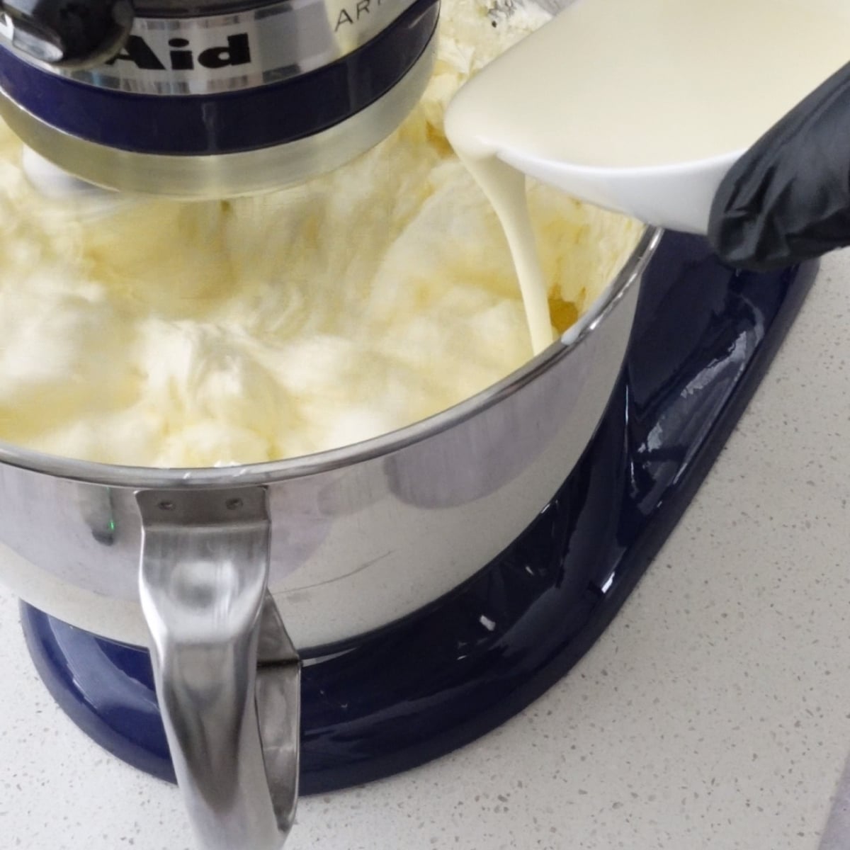 Heavy cream being poured into buttercream in a stand mixer
