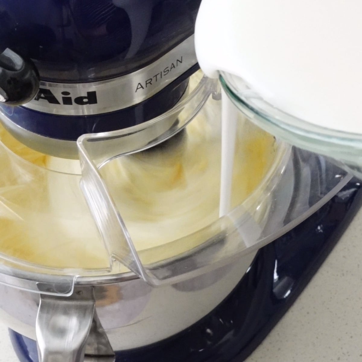 Dissolved sugar mixture being poured into whipped butter in a stand mixer