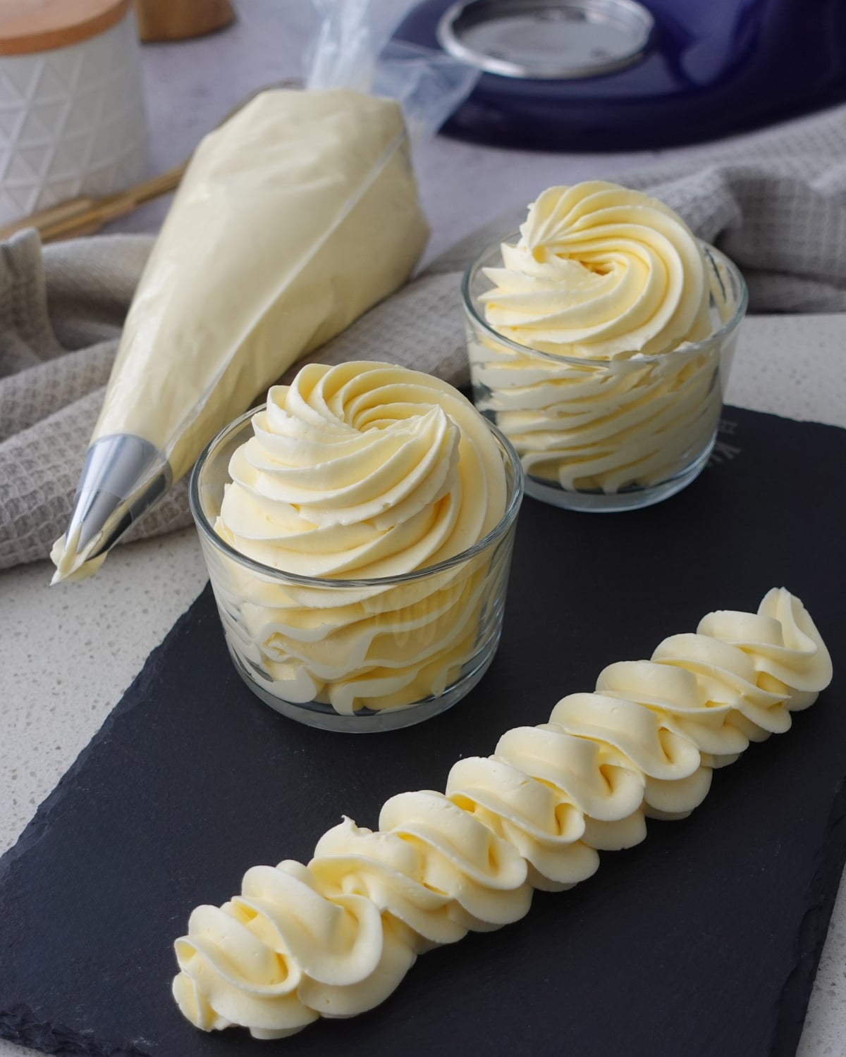 Hot water buttercream piped into swirls in glass jars with a rope border on a slate board