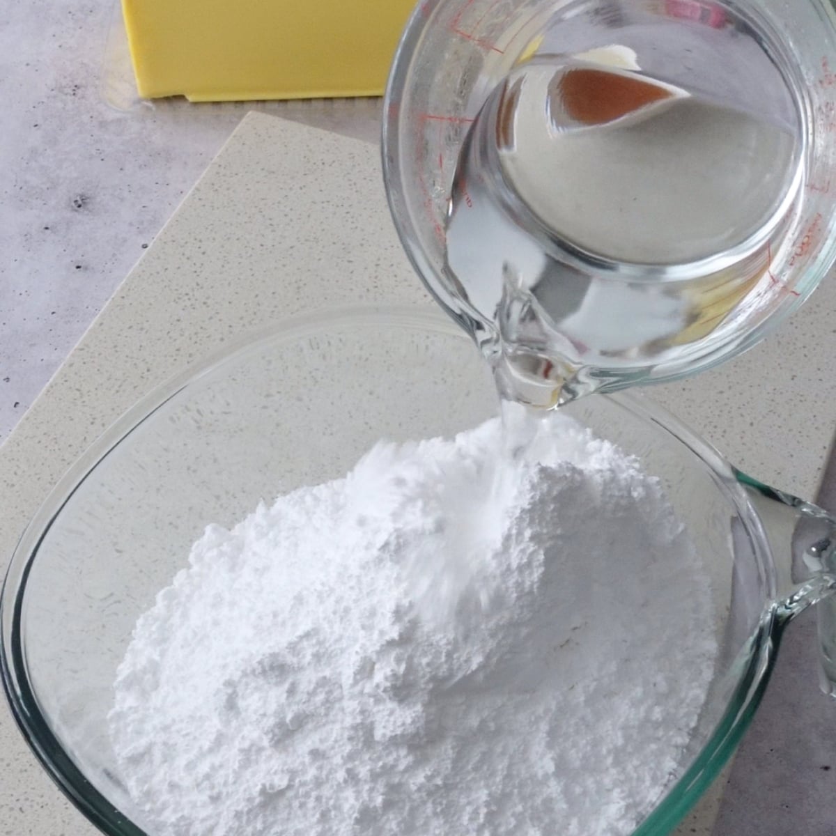 Hot water being poured into powdered sugar and vanilla for hot water buttercream
