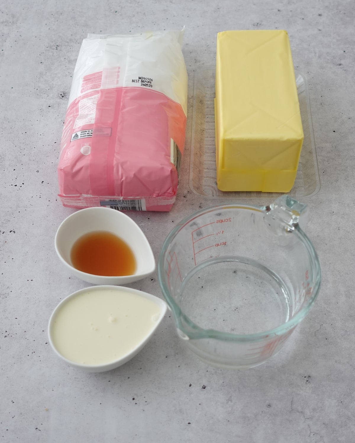 Ingredients for hot water buttercream including butter, powdered sugar, vanilla, and heavy cream on a concrete background