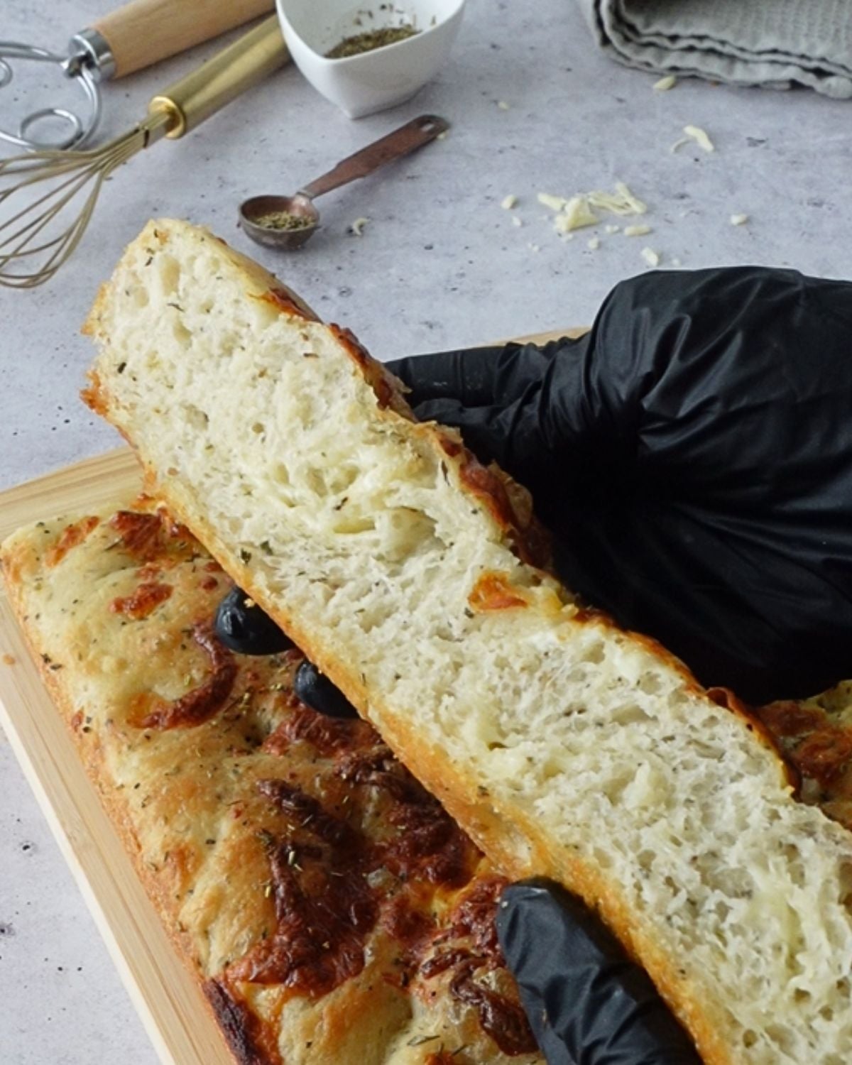 Hand holding a torn slice of same-day herb and cheese focaccia showing the airy crumb