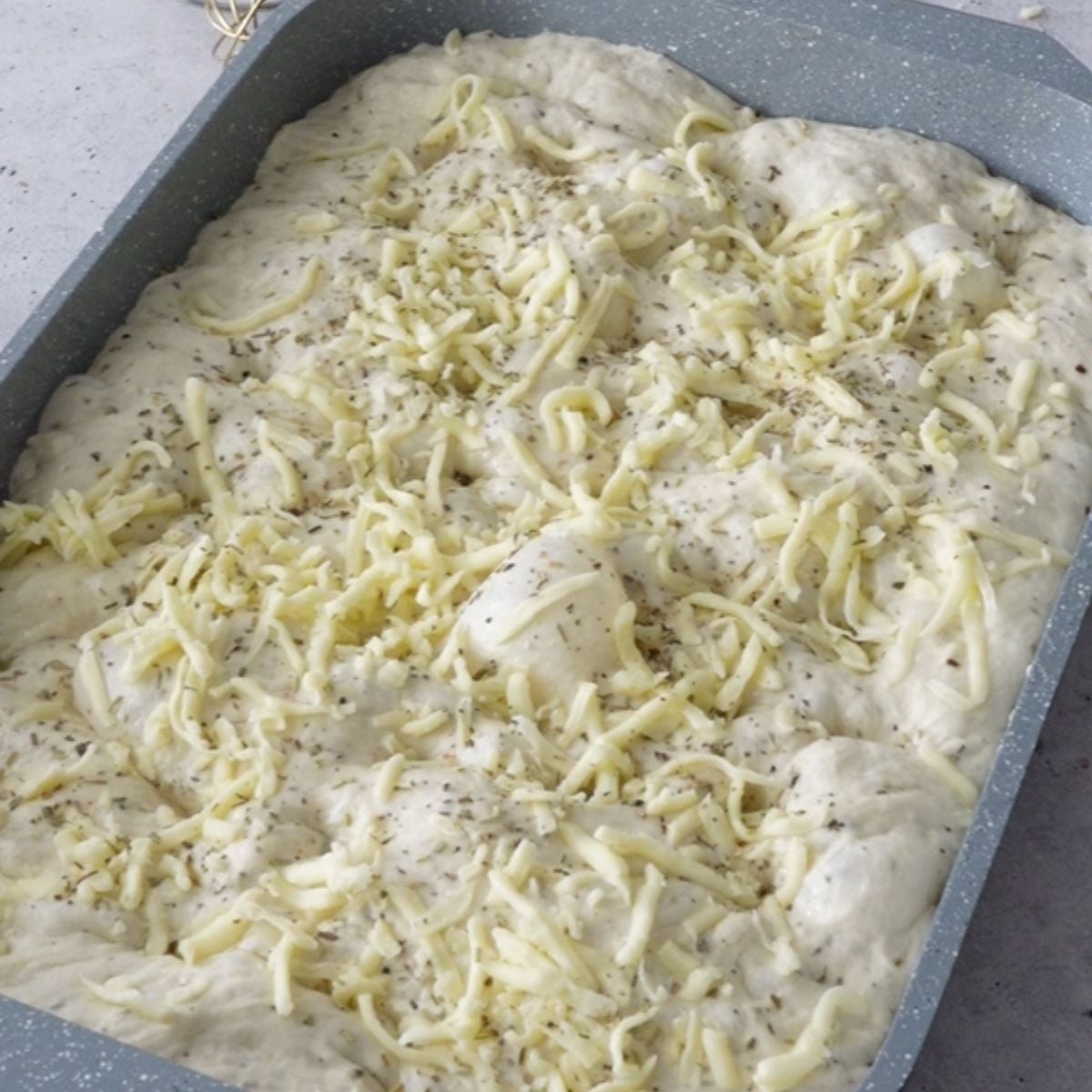 Dimpled focaccia dough topped with mozzarella and herbs before baking