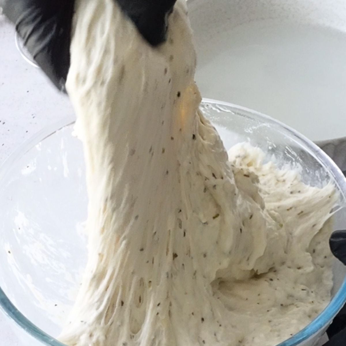 Hands stretching and folding focaccia dough in a bowl